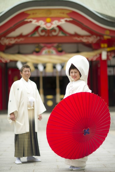 神社の境内で、白無垢姿の花嫁が和傘をさして撮影