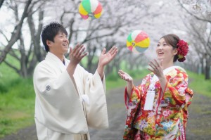 桜並木をバックに紙風船で遊ぶ和装姿の新郎新婦